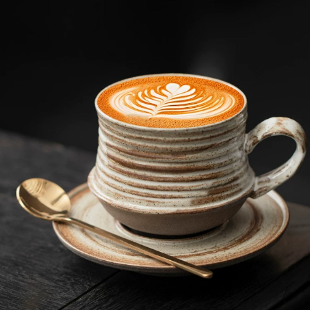 Brown and cream brushed-glaze ceramic coffee cup and saucer with a latte and gold spoon