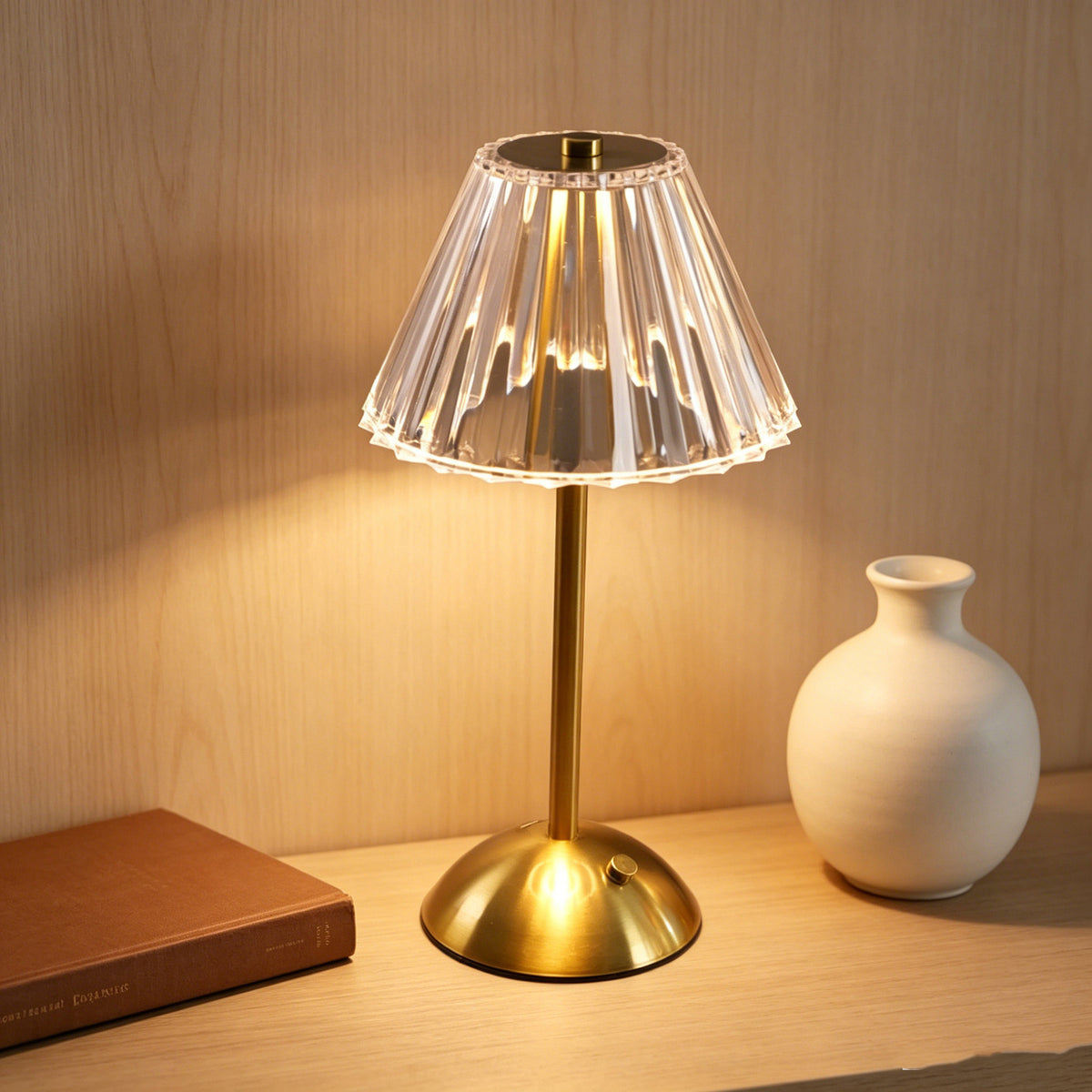 Brass-tone rechargeable table lamp with a clear fluted shade beside a white vase