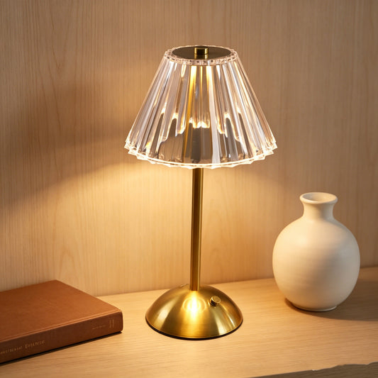 Brass-tone rechargeable table lamp with a clear fluted shade beside a white vase